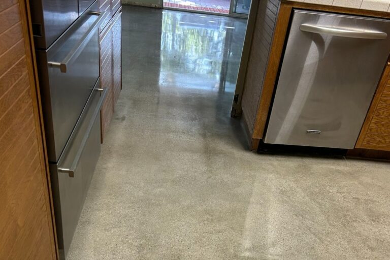 Polished concrete kitchen floor replacing previous tile flooring, creating a seamless, modern look that complements stainless steel appliances and wooden cabinetry.