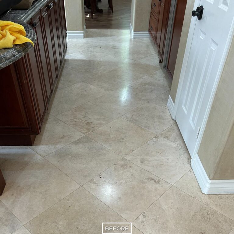 Before travertine floor restoration in San Clemente kitchen, showing dull and stained tiles near cabinets and countertops.
