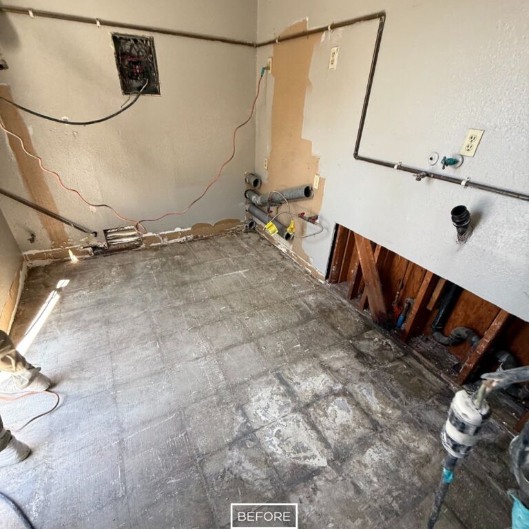 Concrete floor with old flooring residue and exposed wall studs, showing surface damage before restoration work.