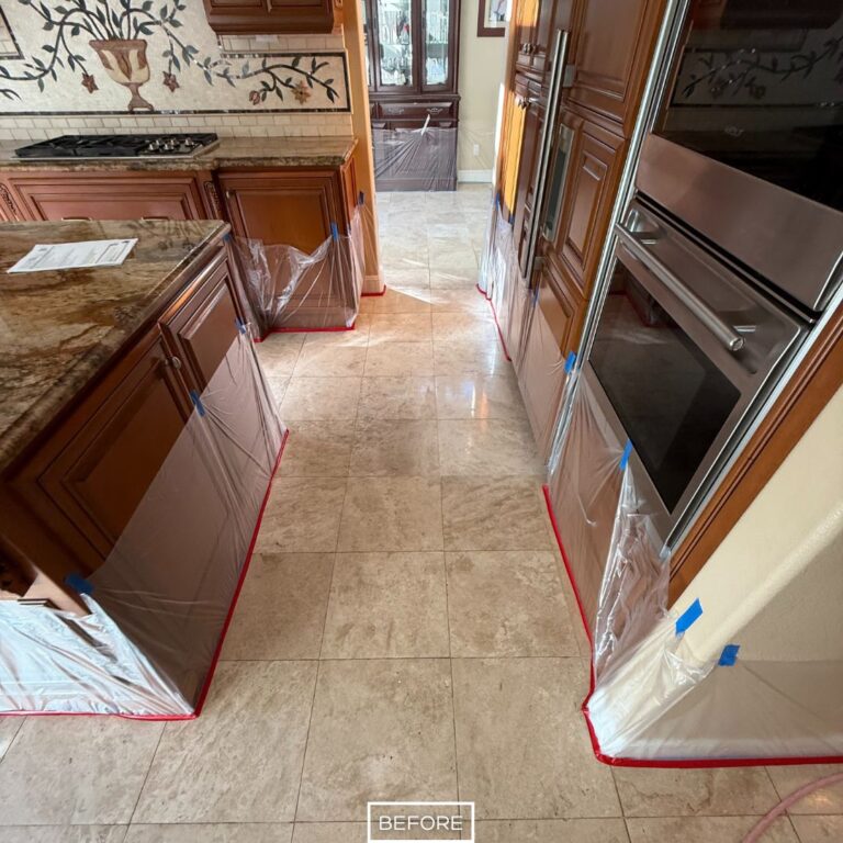 Worn travertine flooring in a Beverly Hills kitchen walkway, with cabinets protected in preparation for stone restoration work.